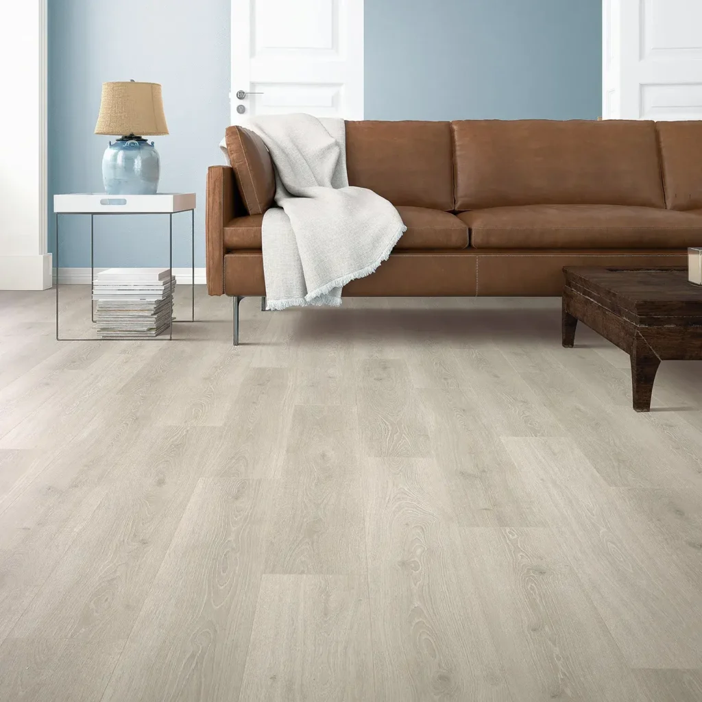 Living room with brown leather sofa and side table lamp on pale grey wood-look Mohawk RevWood Select Boardwalk Collective laminate flooring