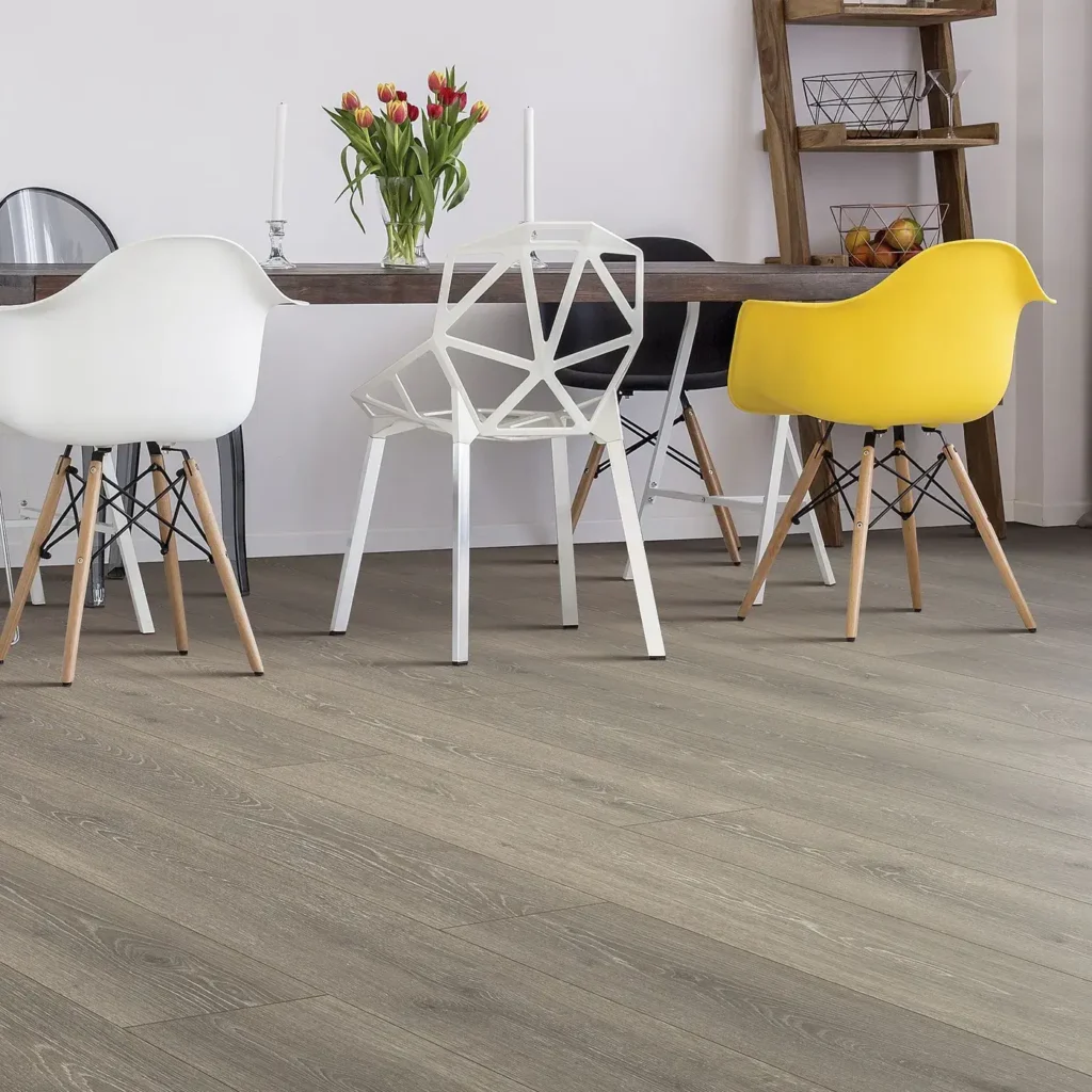 Dining area with white, wire and yellow modern chairs on grey wood-look Mohawk RevWood Select Boardwalk Collective laminate flooring