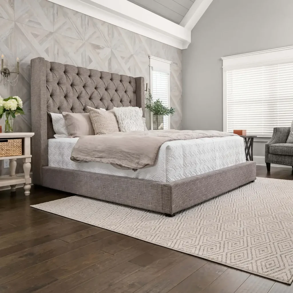 Bedroom with gray tufted bed on a neutral diamond-pattern Shaw Floors Diamonds Forever area rug over wood flooring