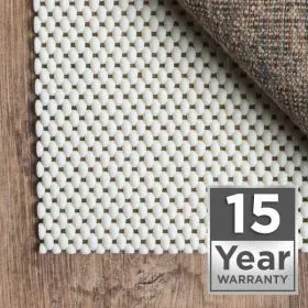White grip rug pad under an area rug on wood flooring with 15 Year Warranty badge
