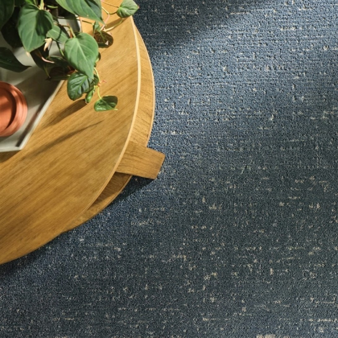Blue Shaw carpet with a round wooden side table and plant